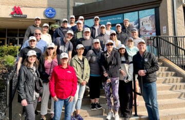 A group of people in Halifax gather on outdoor steps in front of a Marriott hotel, wearing matching white caps as they prepare for a charity walk supporting Homes for Heroes.