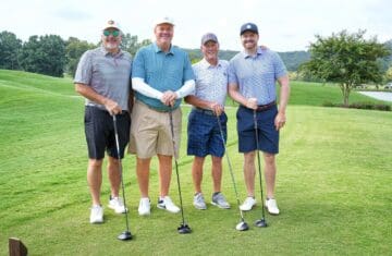 four golfers standing on the green with their golf clubs